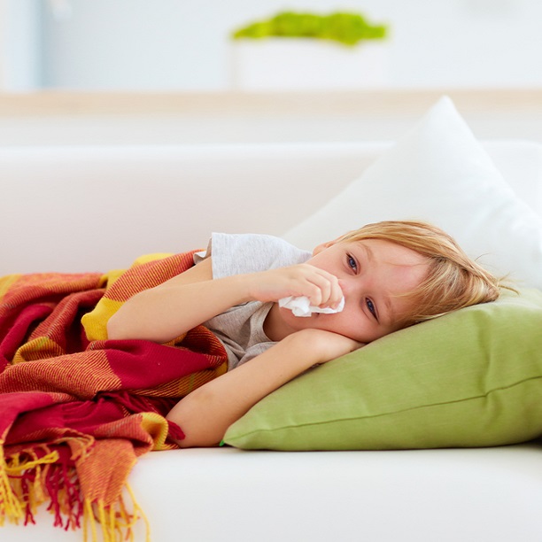 Ett barn som ligger ner på en soffa och håller en näsduk mot näsan